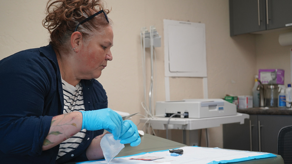 Woman seated in a clinic exam room prepping medical equipment