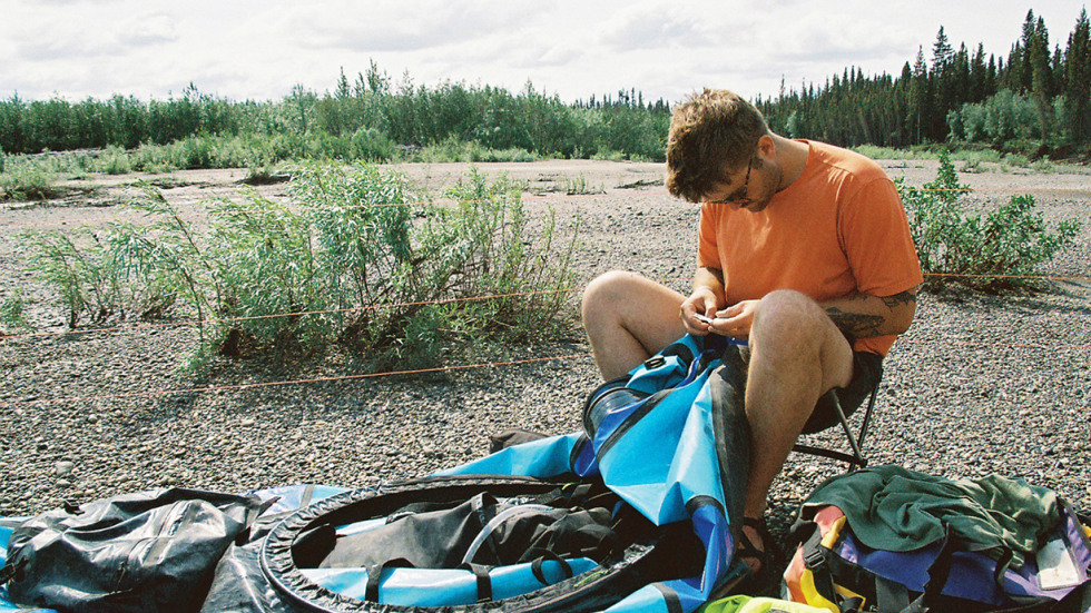 Man seated and repairing a inflatable raft.