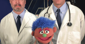 Scott A. Allen MD'91, professor of medicine at the University of California, Riverside, left, and Josiah Rich, MD, MPH, professor of medicine at Alpert Medical School, with Alex, a Sesame Street character whose father is in jail. Rich and Allen wrote in the Annals of International Medicine in October 2014 that "if incarceration has become such a common like experience that it has a home on Sesame Street," then physicians and policymakers can no longer ignore its impact on economic and health inequality.