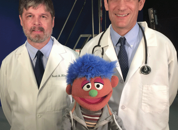 Scott A. Allen MD'91, professor of medicine at the University of California, Riverside, left, and Josiah Rich, MD, MPH, professor of medicine at Alpert Medical School, with Alex, a Sesame Street character whose father is in jail. Rich and Allen wrote in the Annals of International Medicine in October 2014 that "if incarceration has become such a common like experience that it has a home on Sesame Street," then physicians and policymakers can no longer ignore its impact on economic and health inequality.