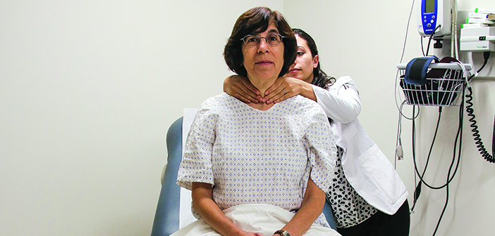 DON’T: Elisseou demonstrates a traditional thyroid exam, where the physician comes from behind the patient and wraps her hands completely around the neck, which can trigger sensations of violent choking. Photo by Jared DiChiara