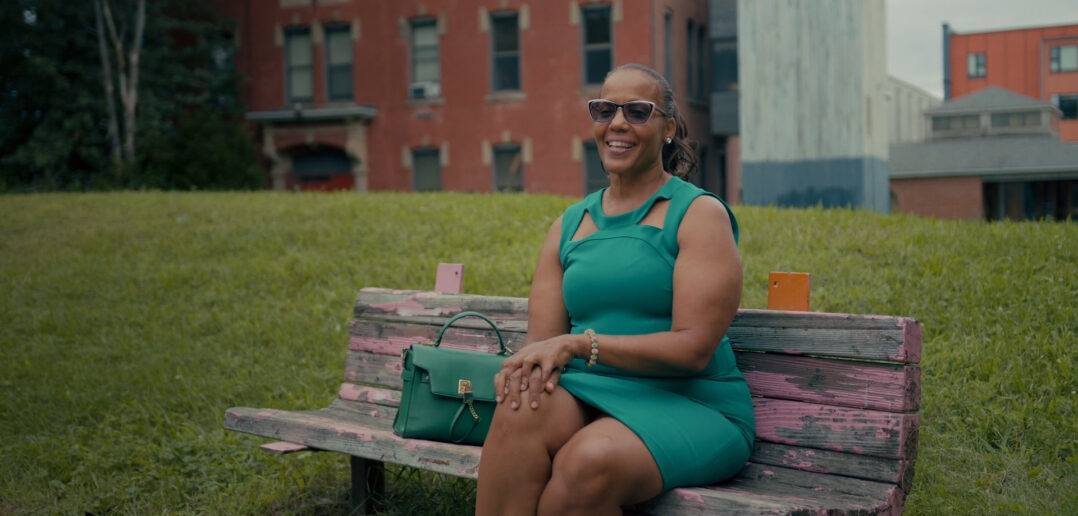 Rochelle Ives, administrative program manager and executive assistant to the vice president of Dining Services, sits on a bench while he is interviewed outside of the John Hope Settlement House in Providence.