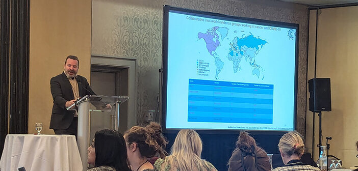 Jeremy Warner, MD, MS, associate director of data science at the Legorreta Cancer Center, stands a podium while next to a slideshow presentation as he addresses a seated crowd at the 2024 Collaboration for Outcomes Using Social Media in Oncology meeting.